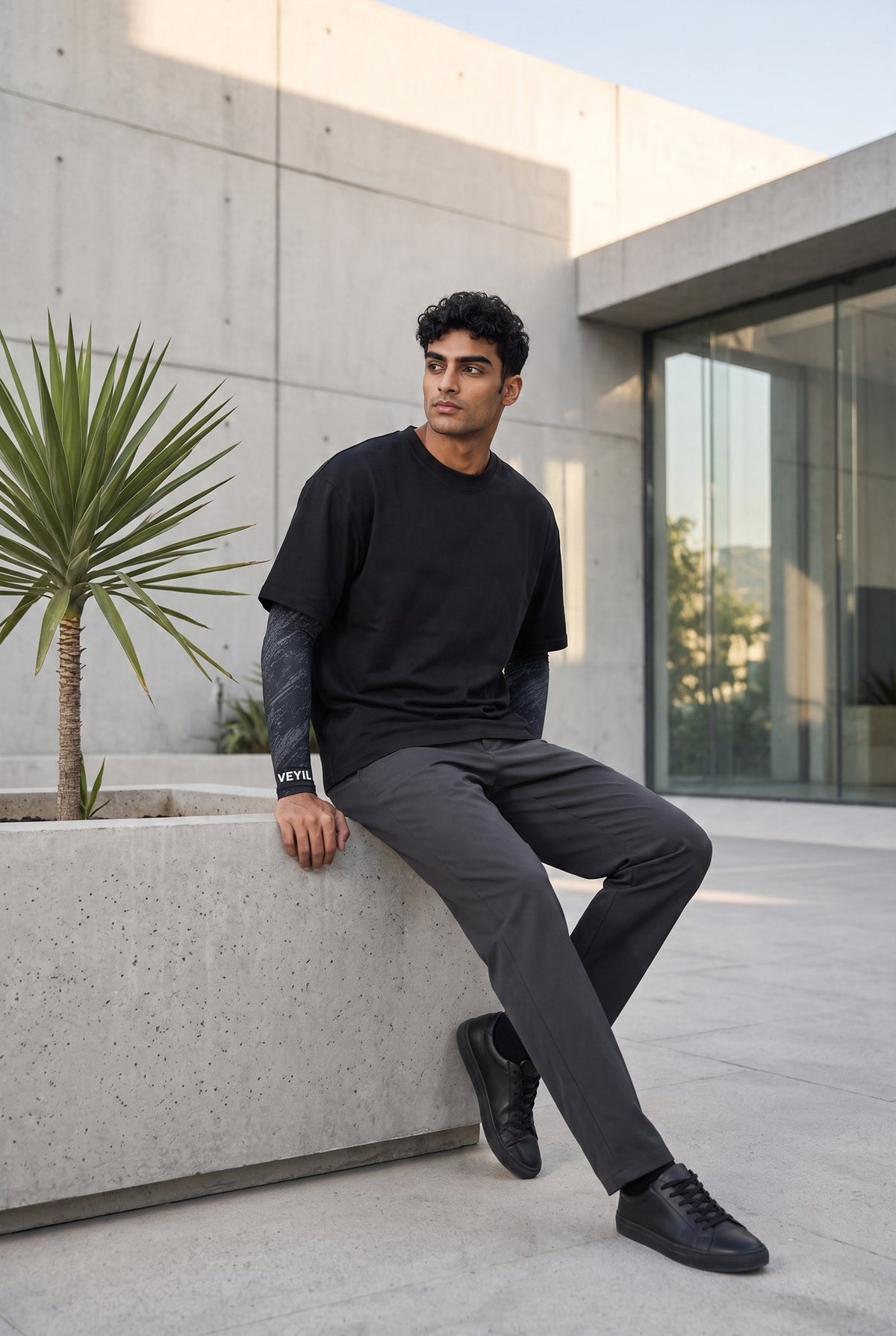 Man seated on a concrete planter wearing black VEYIL UPF 50+ arm sleeves with a T-shirt