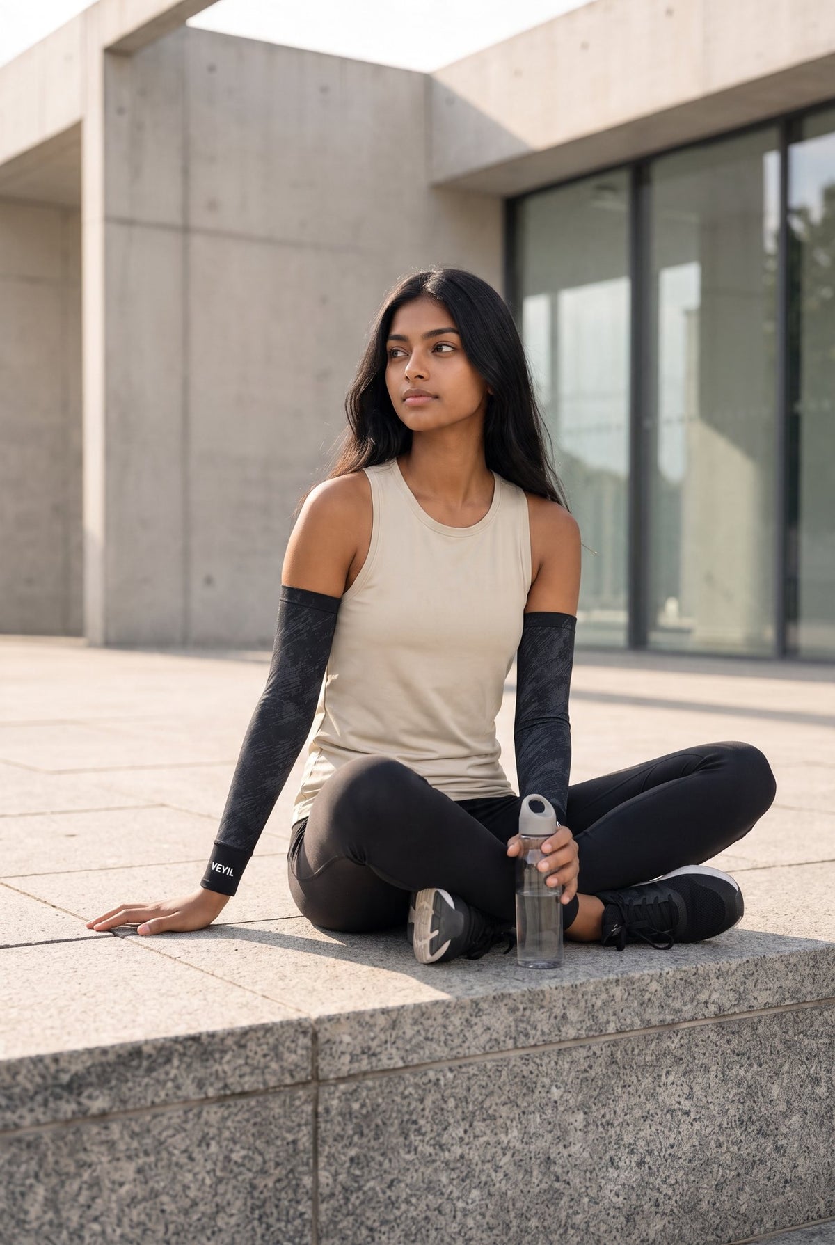 Woman seated outdoors wearing black VEYIL UPF 50+ cooling arm sleeves with a tank top