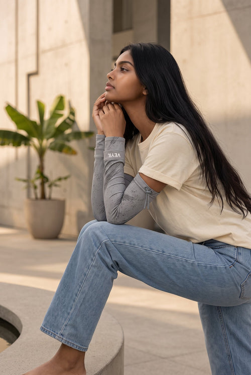 Woman seated outdoors wearing grey VEYIL UPF 50+ arm sleeves with drawstring top, side view